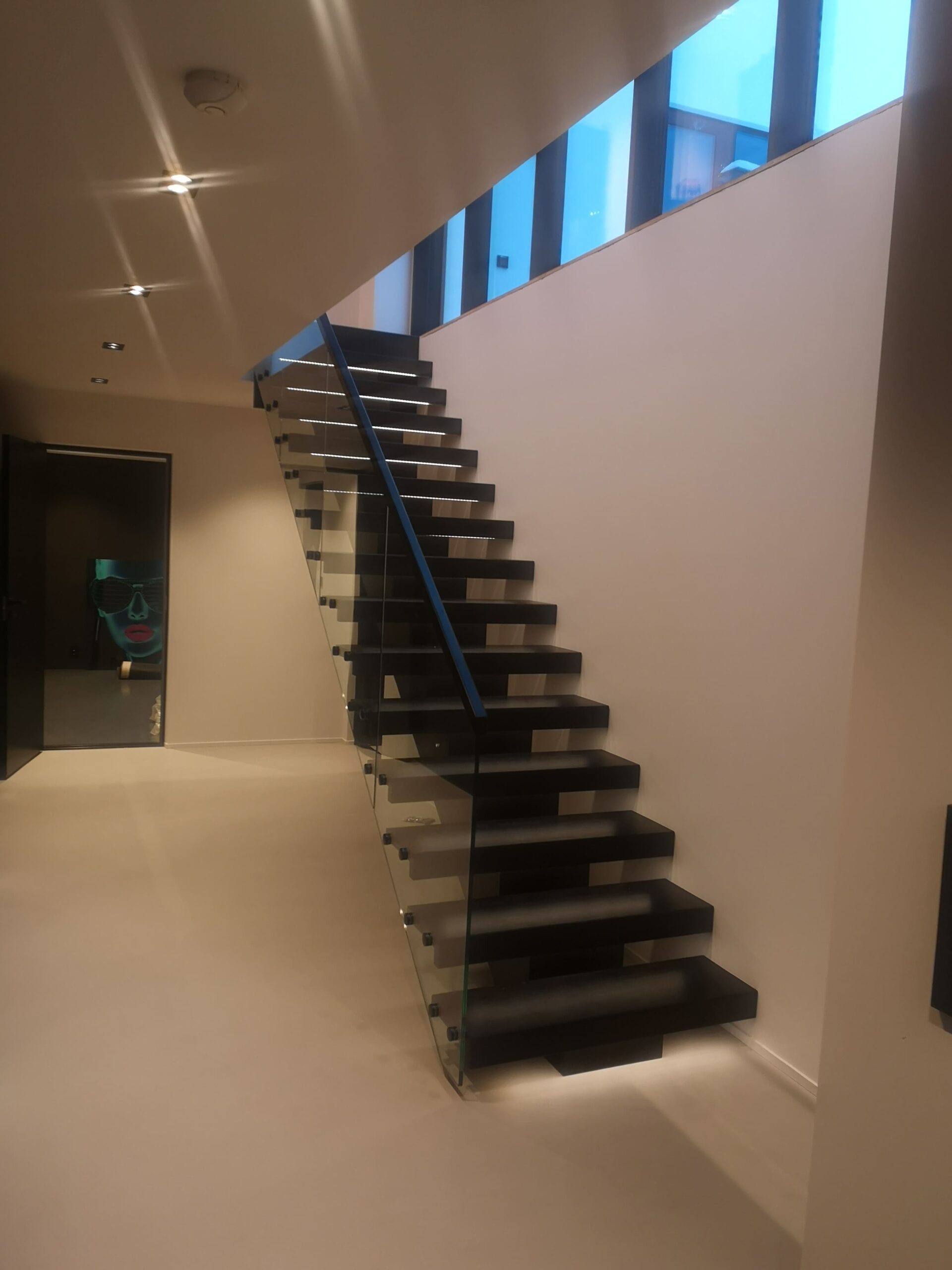 03. A black staircase with a wooden beam and a glass railing with LED lighting